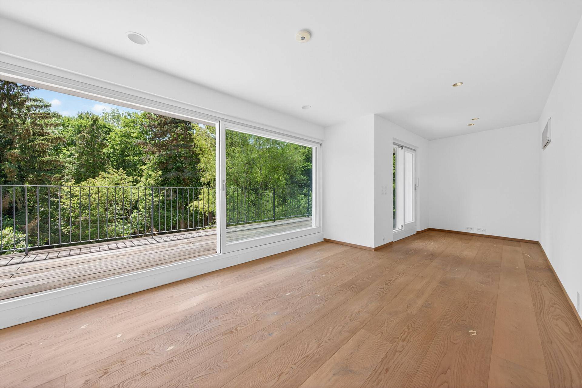 Geräumiges Wohnzimmer mit Holzboden, großen Fenstern und Zugang zu einem Balkon.