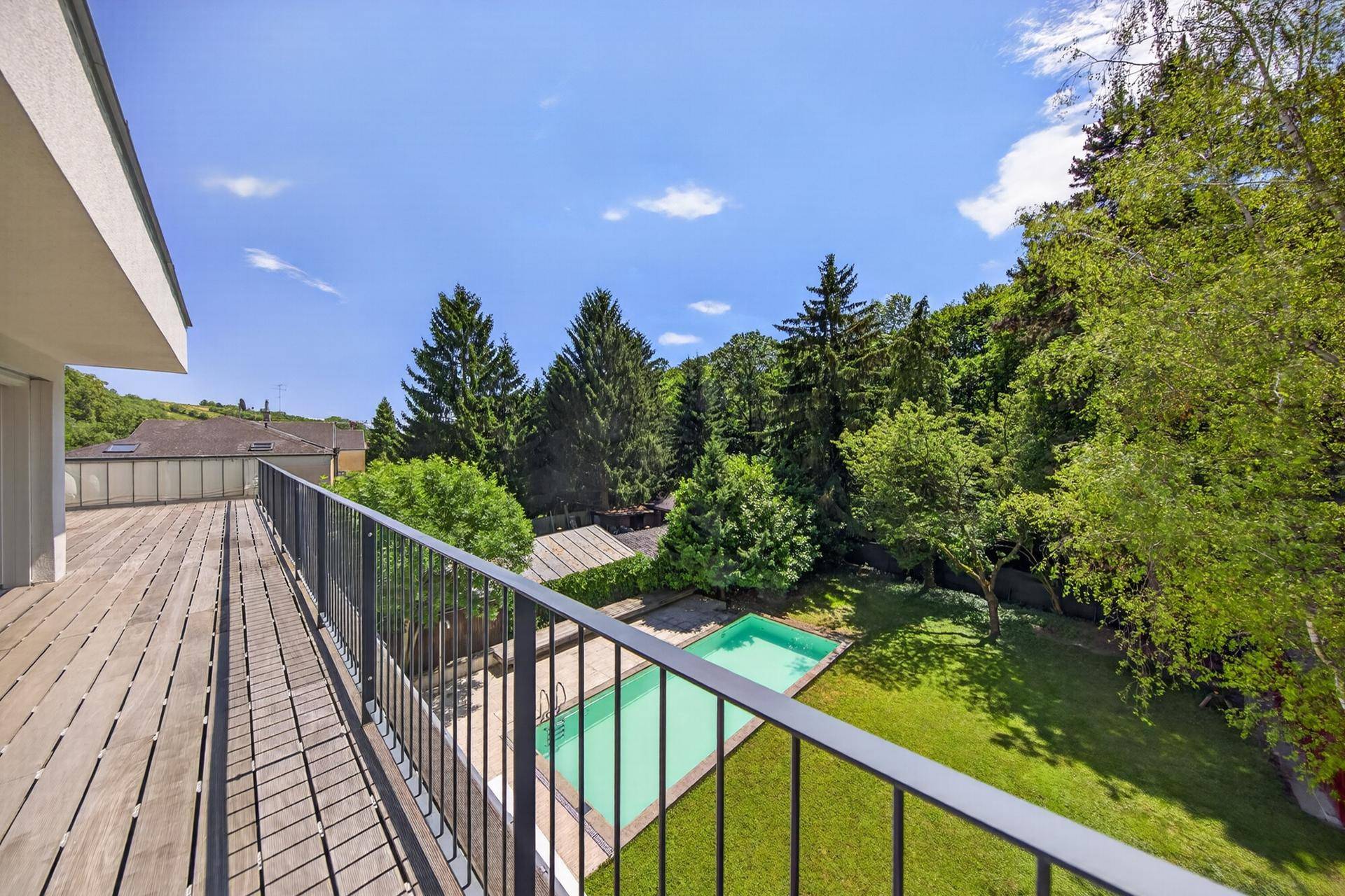 Großer Holzbalkon mit Metallgeländer und weitem Blick über den Garten und die Umgebung.