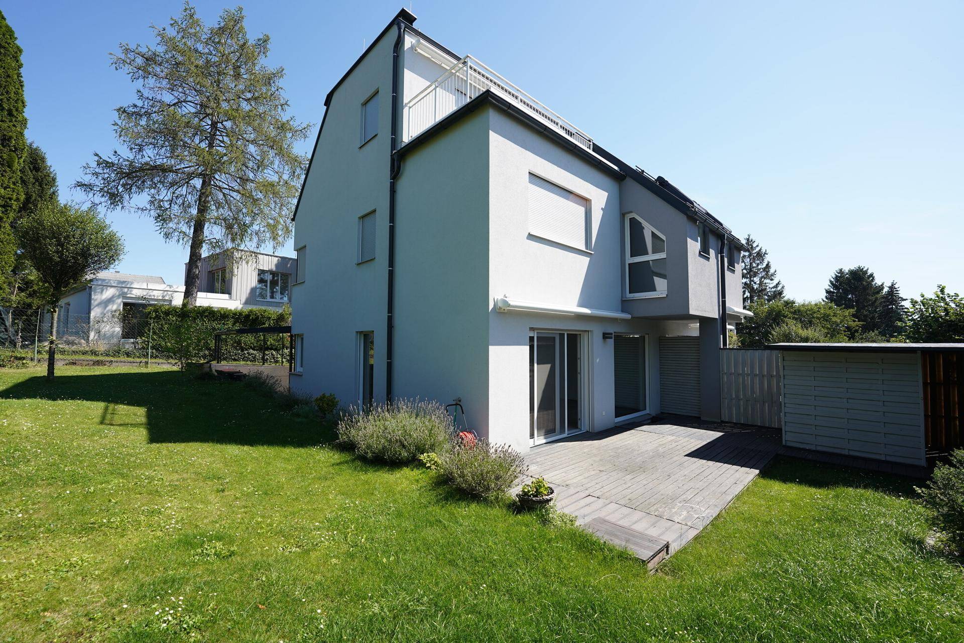 Moderne Hausfassade mit Terrasse und gepflegtem Rasenbereich, umgeben von Grün.