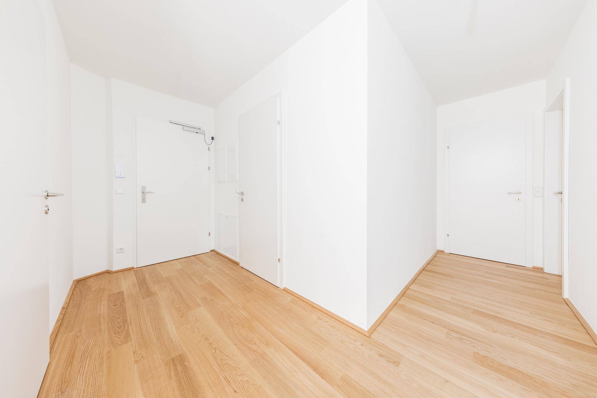 Heller Eingangsbereich mit neuem Holzparkett und weißen Wänden, bereit zur individuellen Gestaltung.