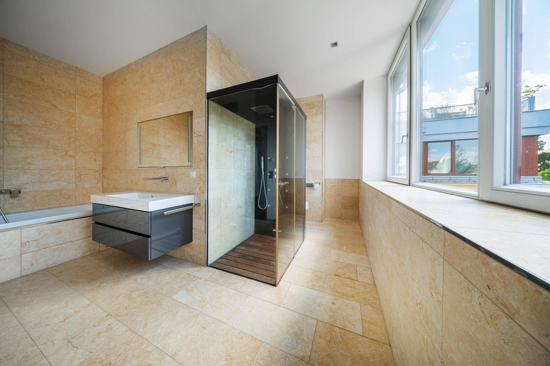 Elegantes Badezimmer mit beigen Fliesen, großer begehbarer Dusche und viel Tageslicht durch die Fenster.