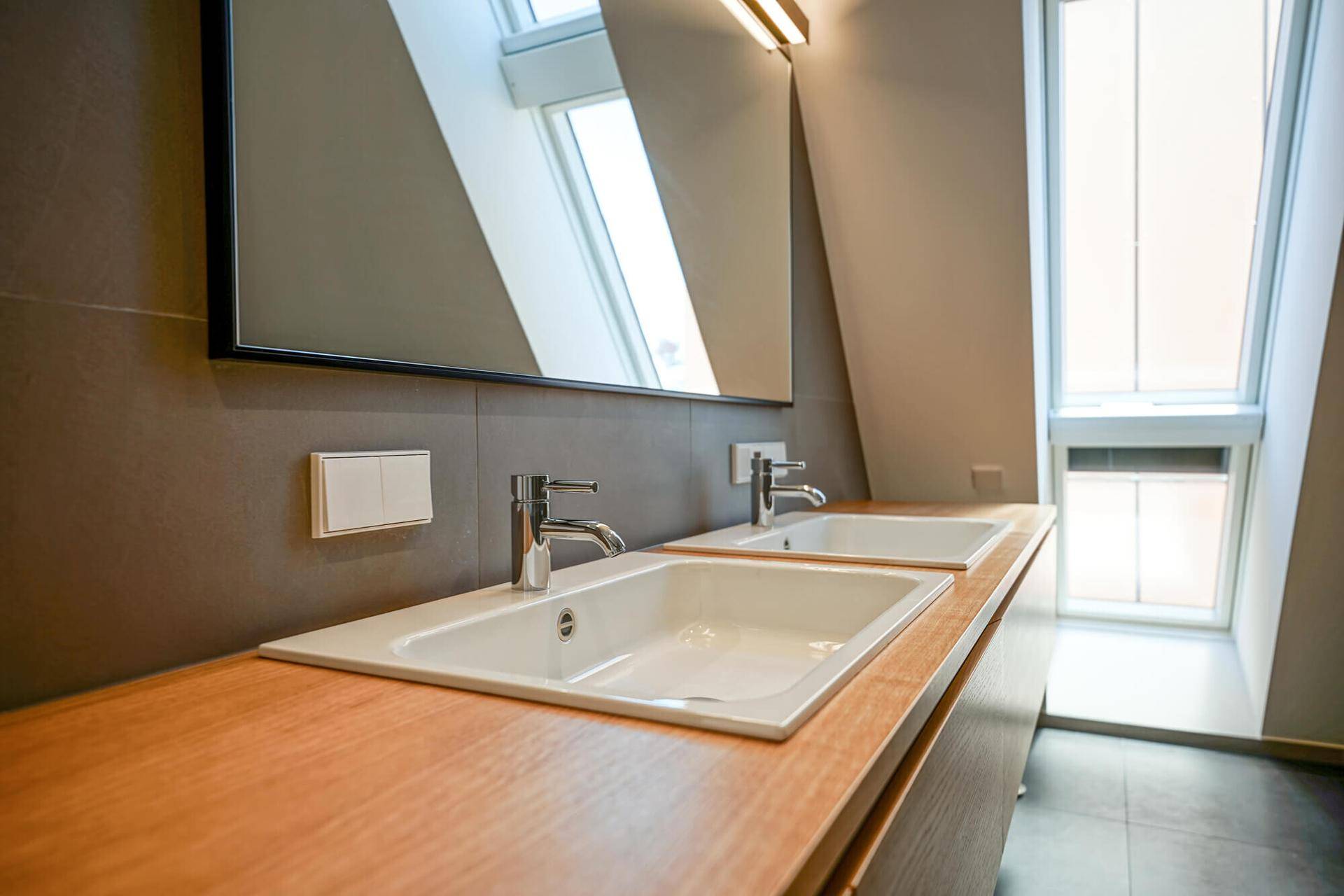 Modernes Badezimmer mit Doppelwaschbecken, Holzplatte und viel Tageslicht durch Dachfenster.