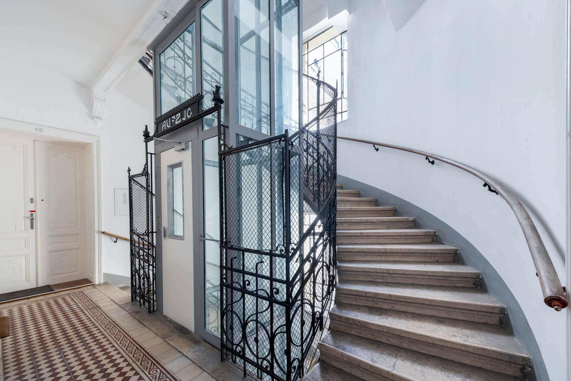 Historisches Treppenhaus mit elegantem Aufzug und schmiedeeisernem Geländer.