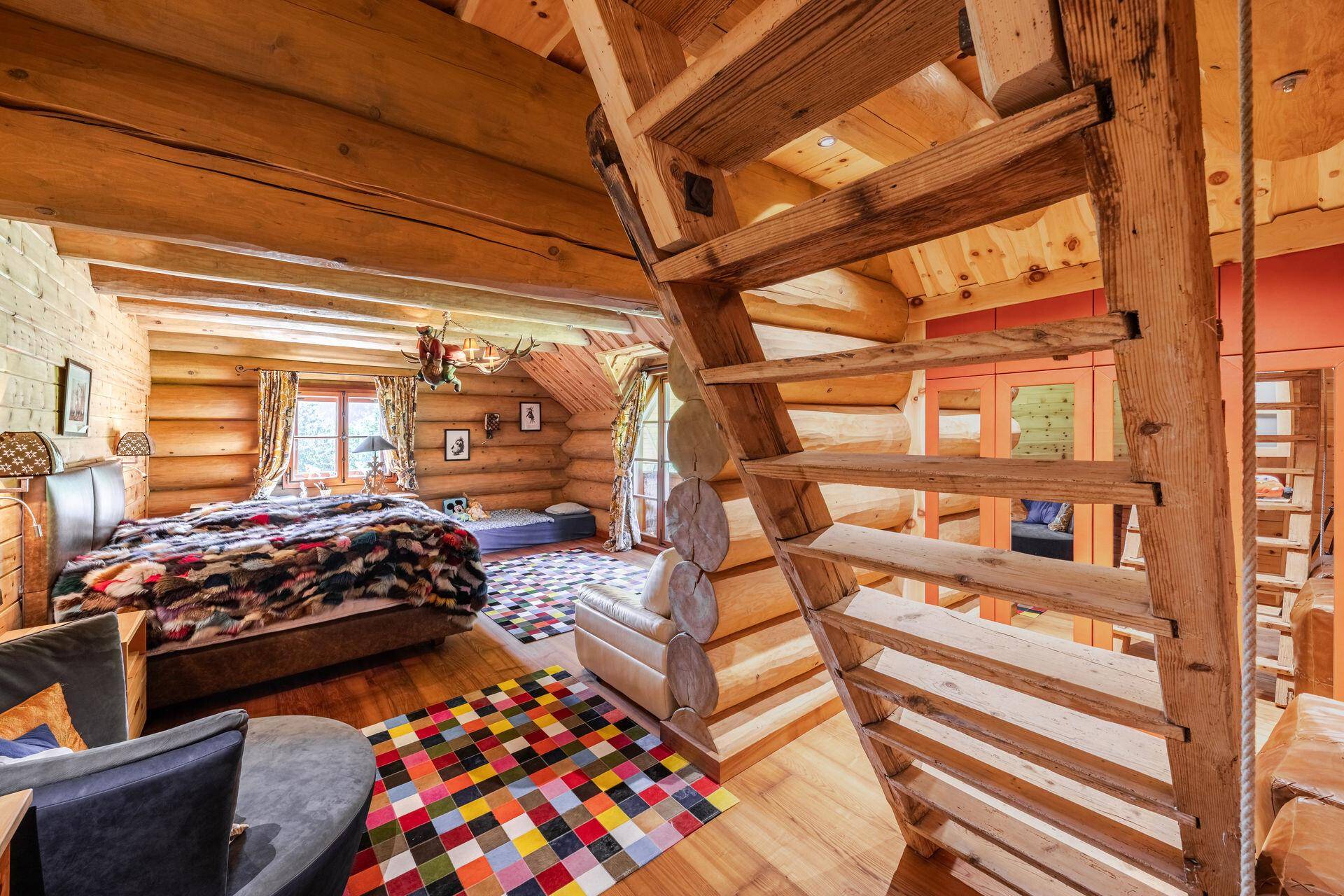 Rustikales Schlafzimmer mit Holzwänden, farbenfrohem Teppich und offener Holztreppe.