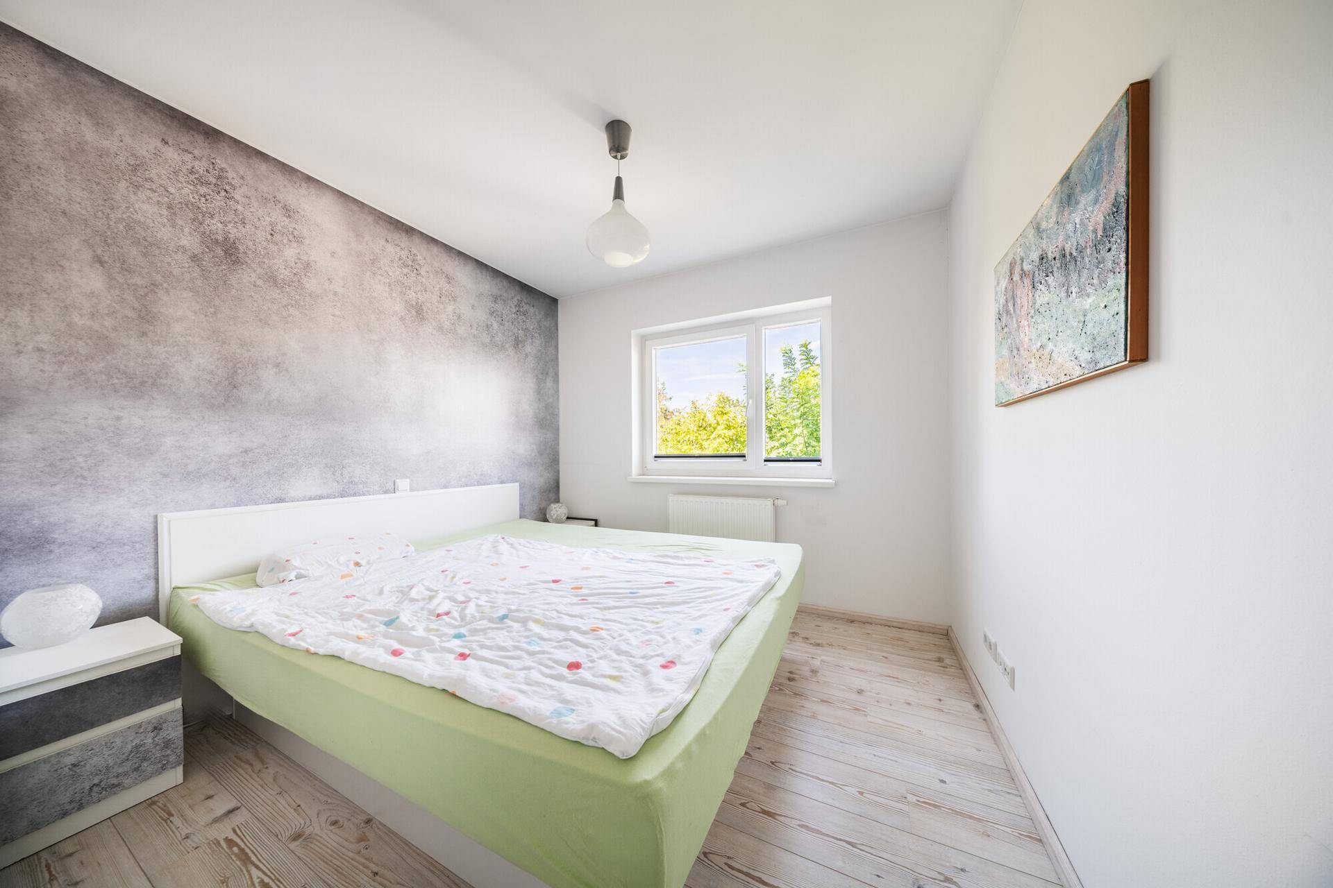 Schlafzimmer mit hellem Holzboden, modern gestalteter Wand und einem großen Bett.