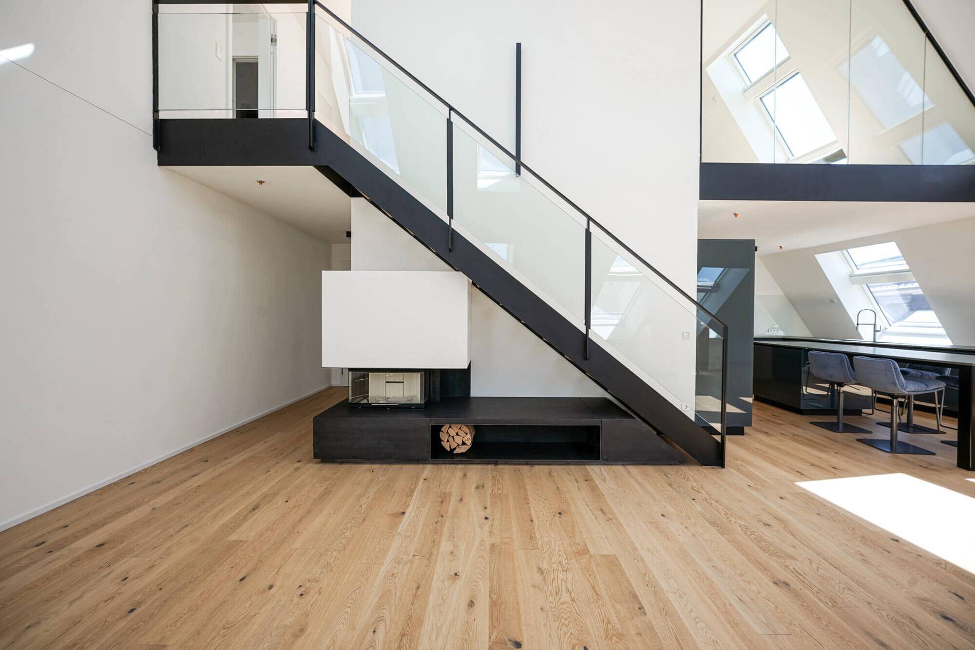 Moderne Treppe mit Glasgeländer und integriertem Kamin mit Holzablage im offenen Wohnbereich.