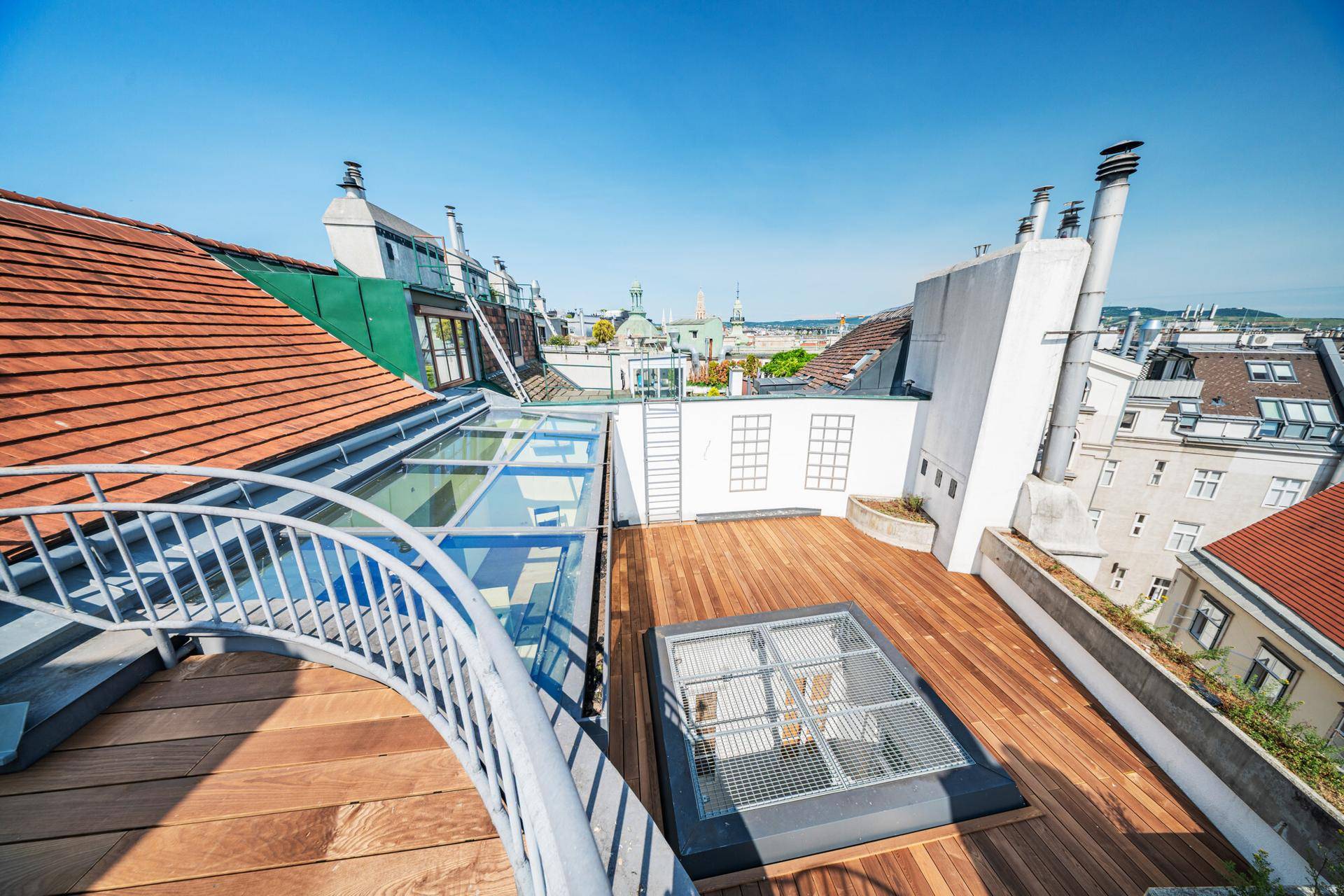Weitläufige Dachterrasse mit Holzdeck und Panoramablick über die Dächer der Stadt.