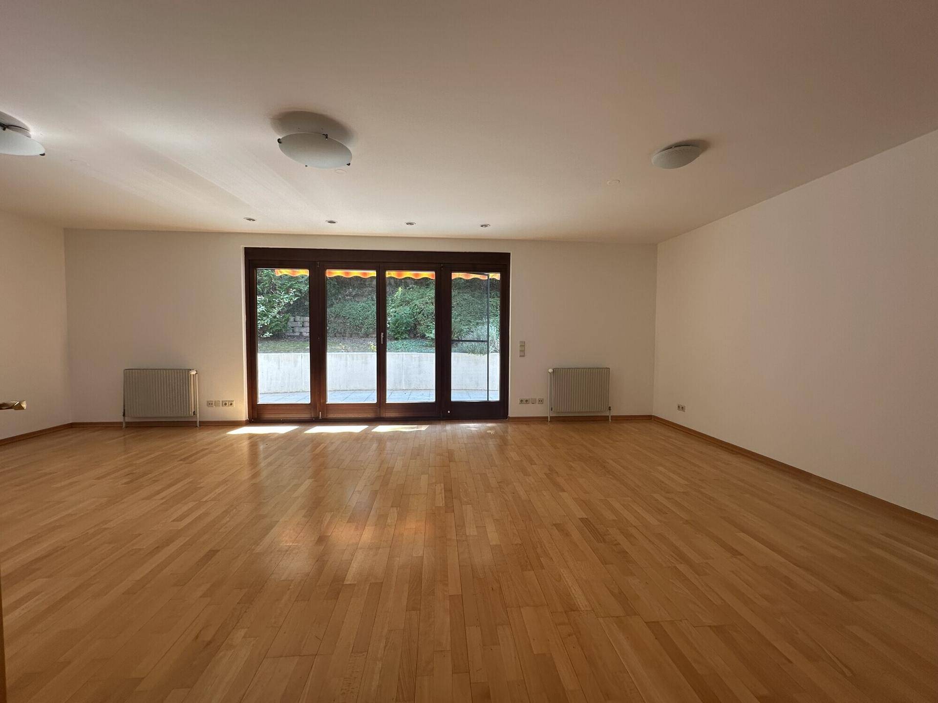 Helles Wohnzimmer mit Holzboden und großen Fenstern, die viel Tageslicht hereinlassen.