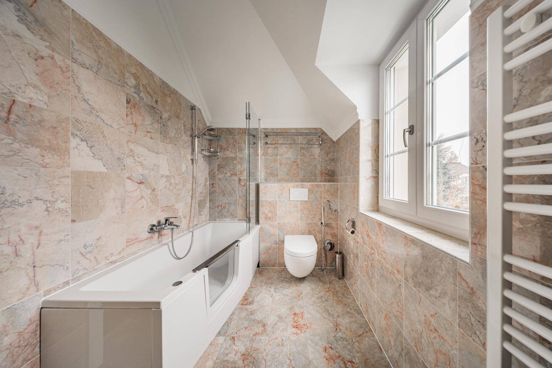 Modernes Badezimmer mit Badewanne, WC, Marmorfliesen und beheiztem Handtuchhalter.