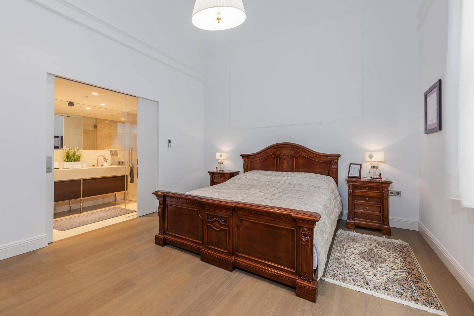 Helles Schlafzimmer mit klassischem Holzbett und direktem Zugang zu einem modernen Bad.