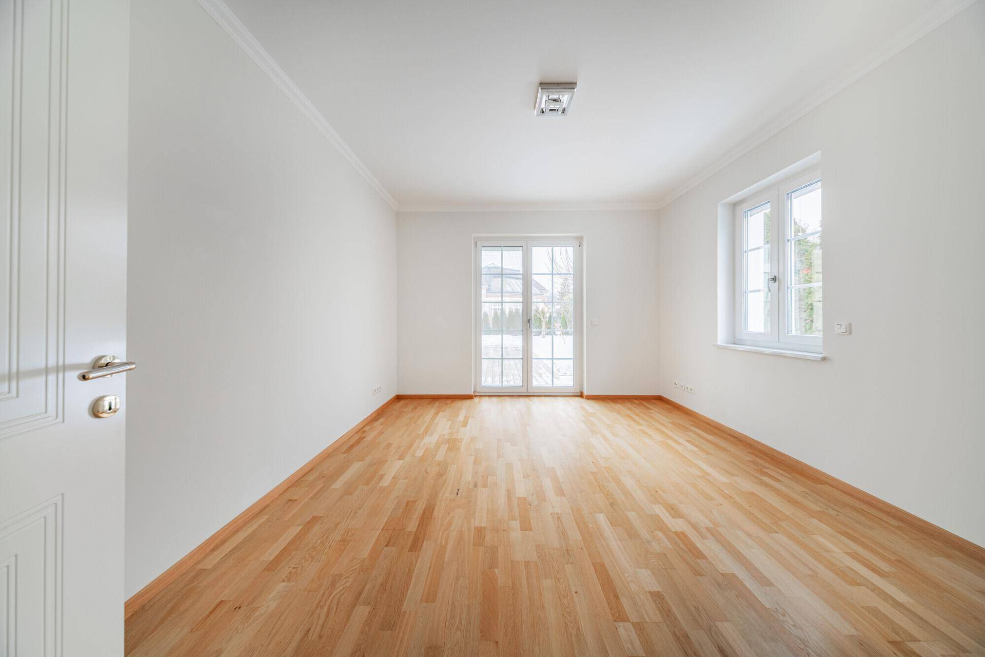 Helles Zimmer mit Holzboden und Zugang zu einem kleinen Balkon oder einer Terrasse.