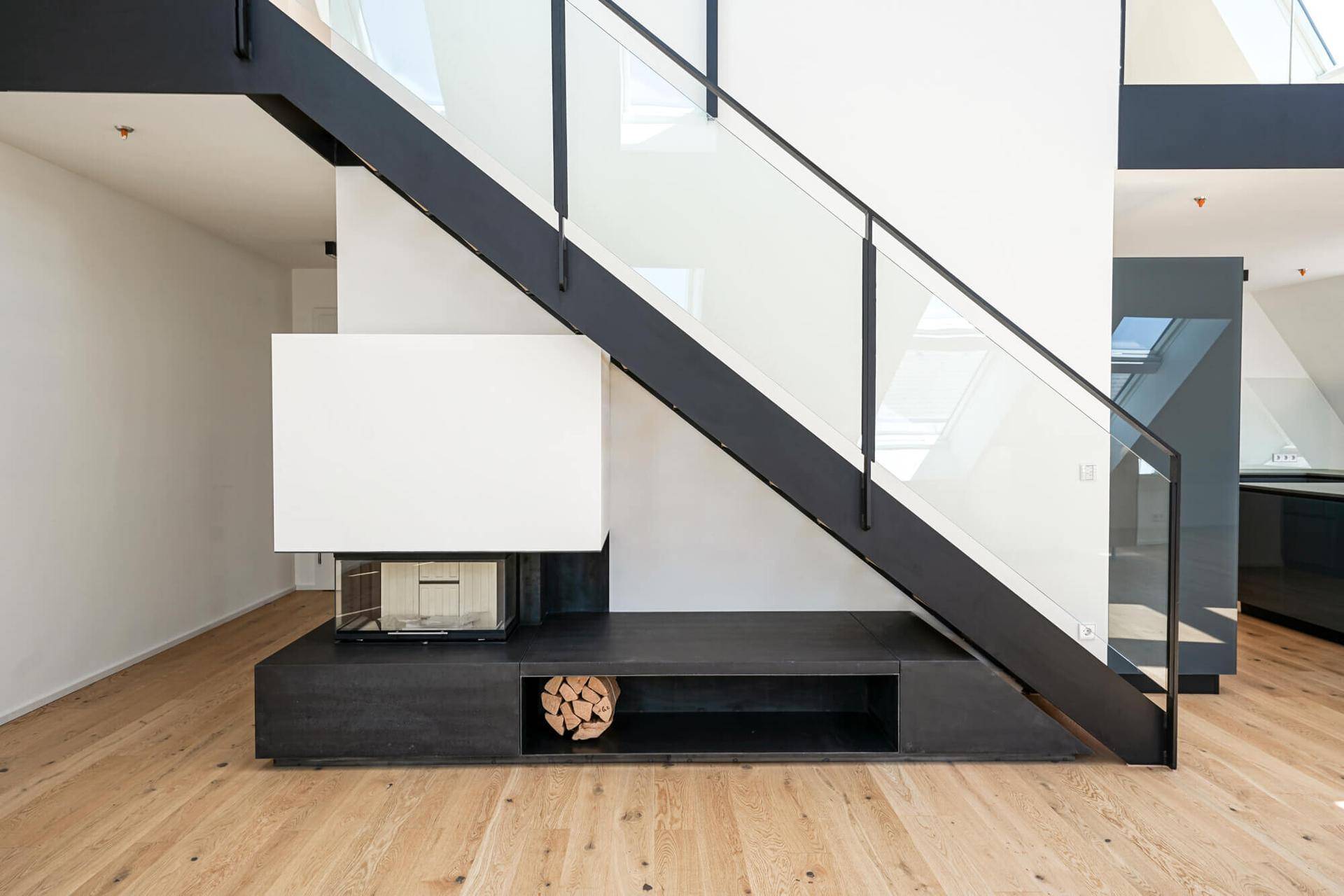Moderne Treppe mit Glasgeländer und integriertem Kamin mit Holzablage im offenen Wohnbereich.