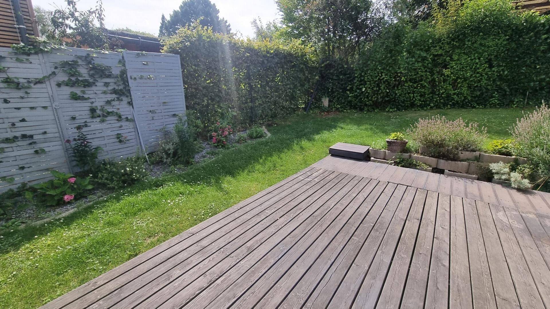 Sonniger Terrassenbereich mit Holzdeck und umgebender Bepflanzung, ideal für Outdoor-Aktivitäten.