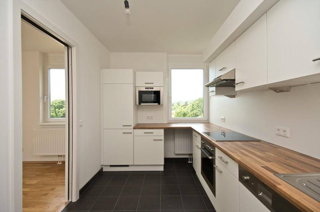 Moderne Einbauküche mit weißen Schränken, Holz-Arbeitsplatte, dunklen Fliesen und integrierten Geräten.