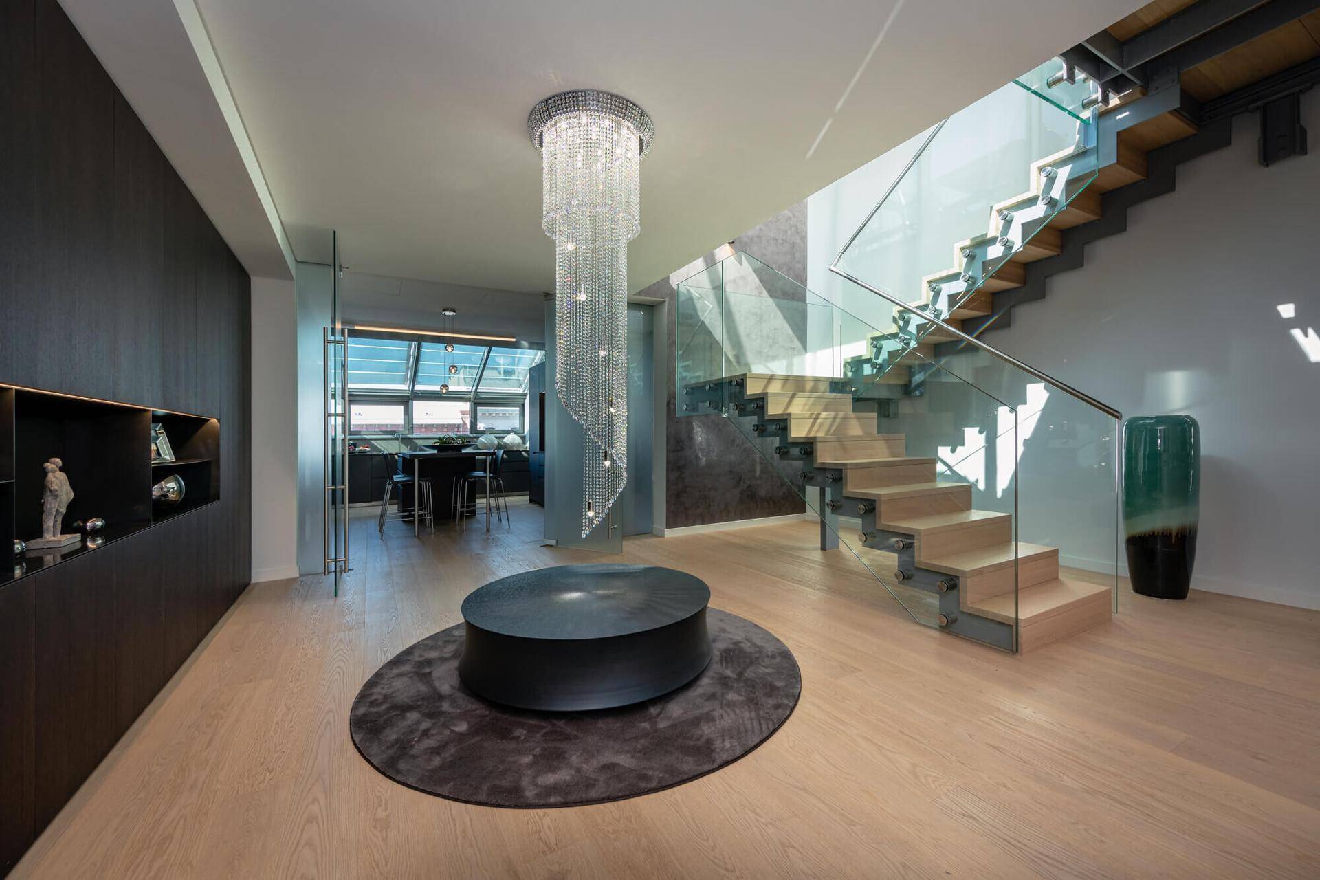 Eleganter Eingangsbereich mit beeindruckendem Kronleuchter und moderner Holztreppe mit Glasgeländer.