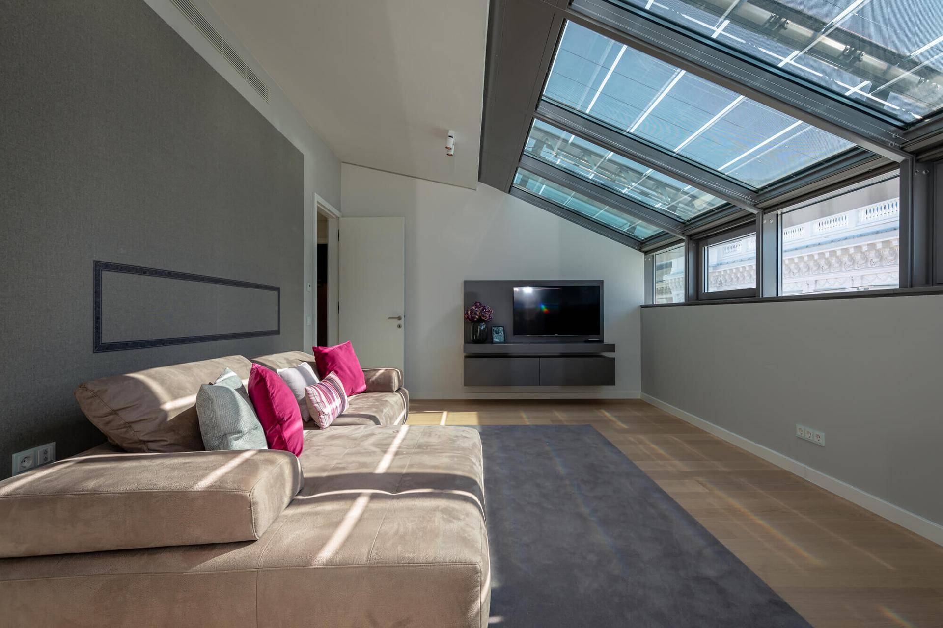 Gemütlicher Wohnbereich mit großem Sofa, Fernseher und schrägem Glasdach für viel Helligkeit.