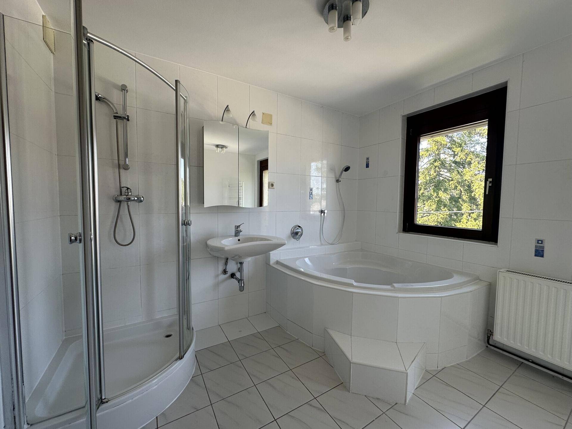 Geräumiges Badezimmer mit weiß gefliesten Wänden, Duschkabine und Eckbadewanne.