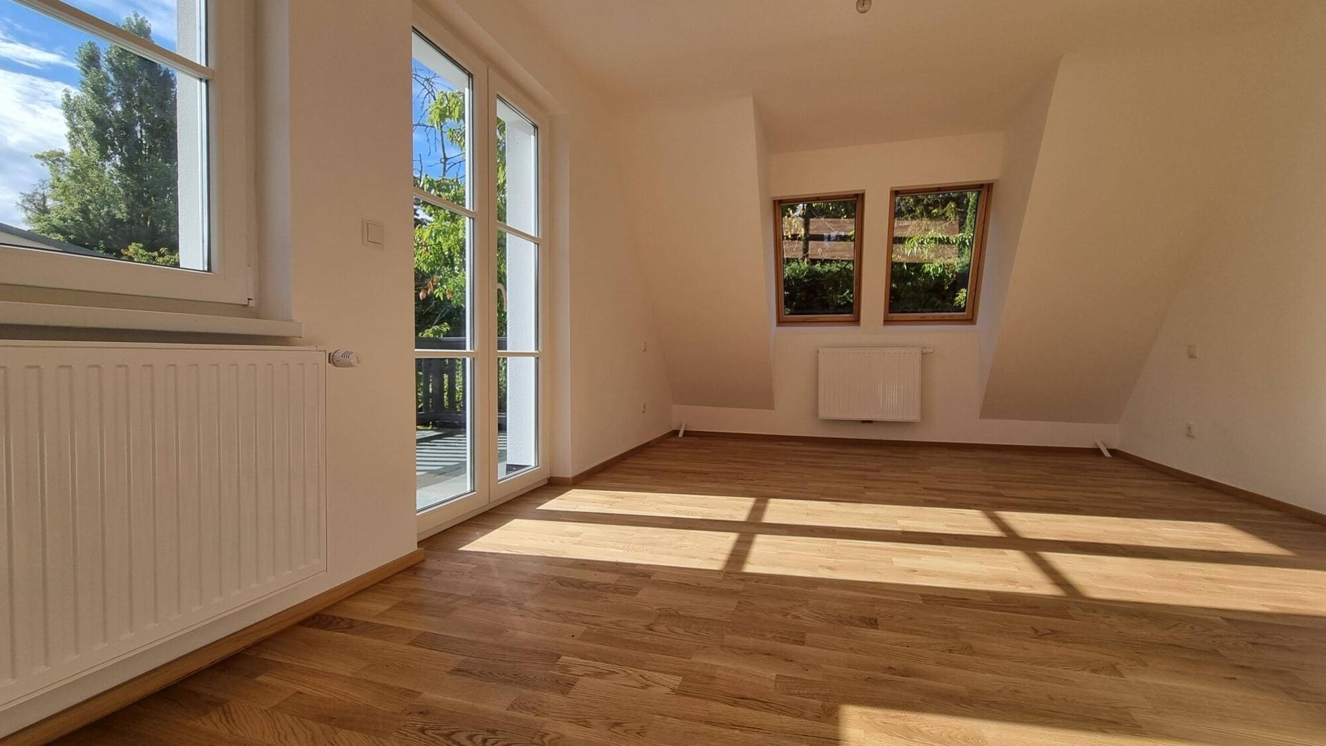 Helles Zimmer im Dachgeschoss mit Holzboden und Zugang zu einem Balkon.