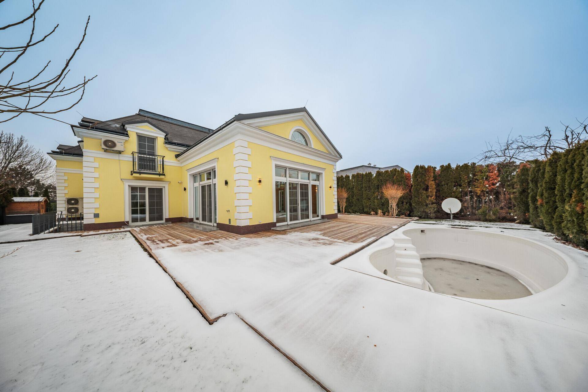 Gelbe Villa mit großer Holzterrasse und eingelassenem Pool im verschneiten Garten.