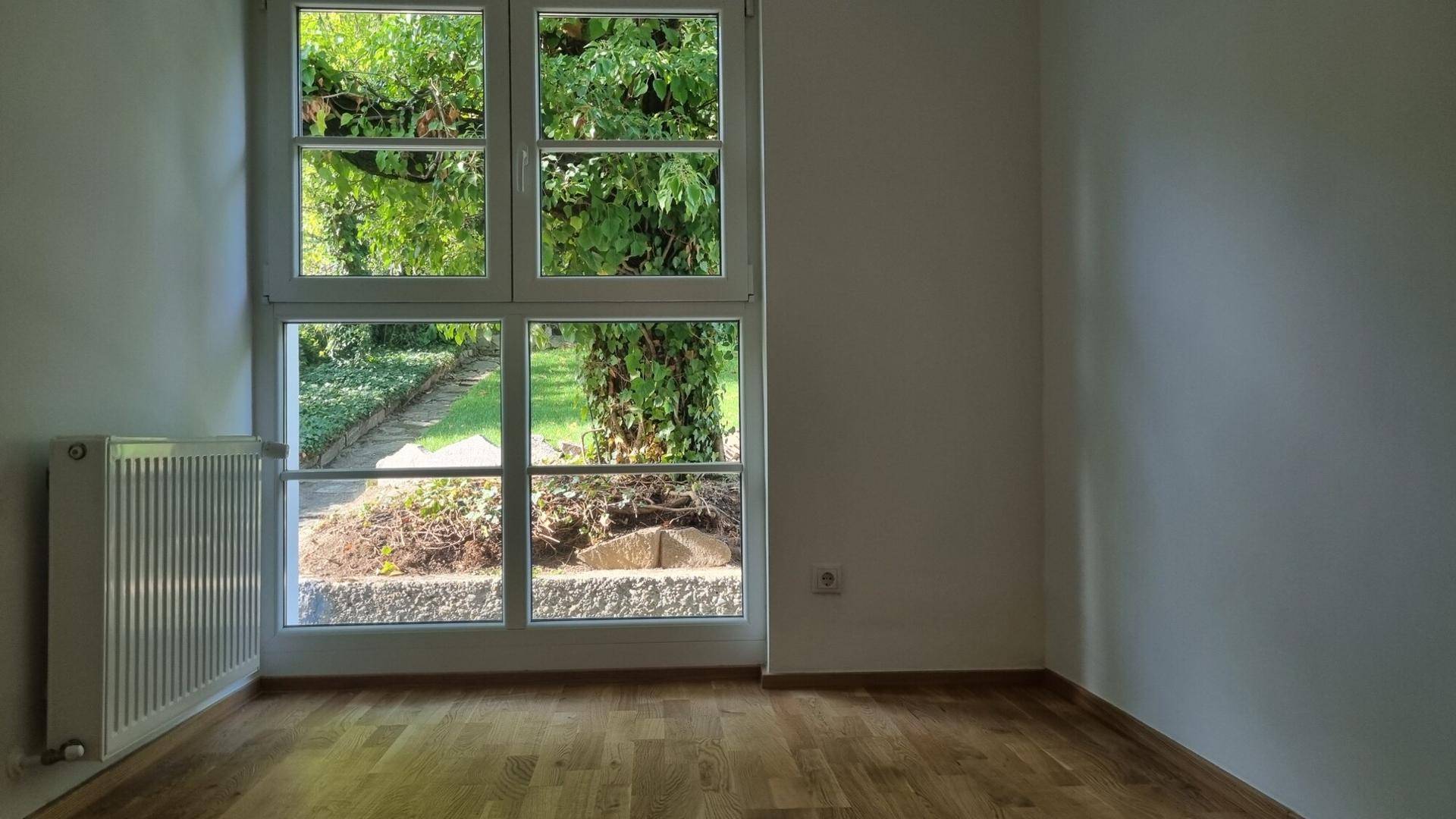 Helles Zimmer mit Holzboden und großem Fenster mit Blick in den Garten.