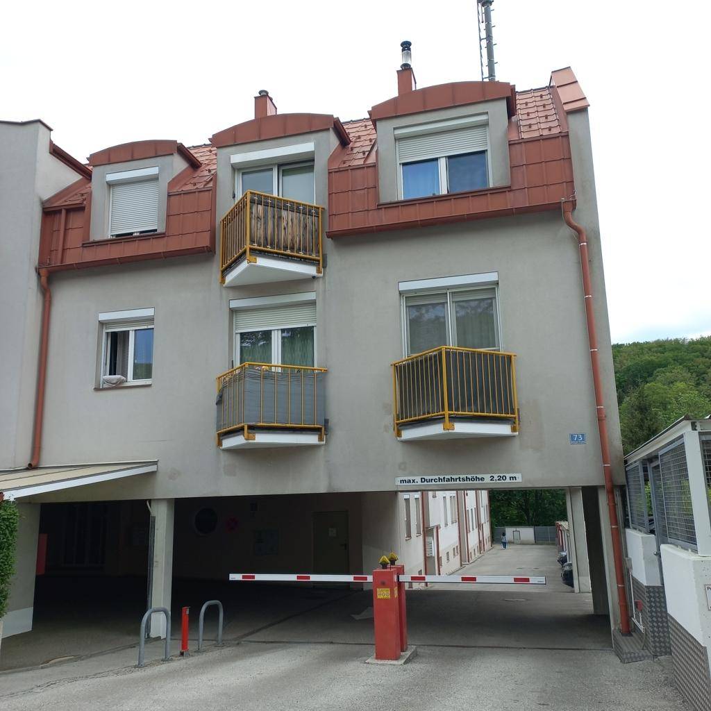 Eingangsbereich zu einer Tiefgarage oder einem Carport mit Schranke und darüberliegenden Balkonen.