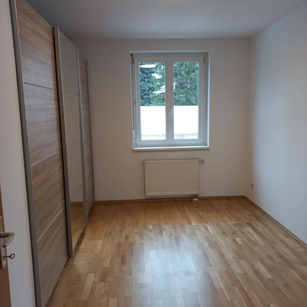 Helles Schlafzimmer mit Holzfußboden, weiß gestrichenen Wänden und einem großen Kleiderschrank.