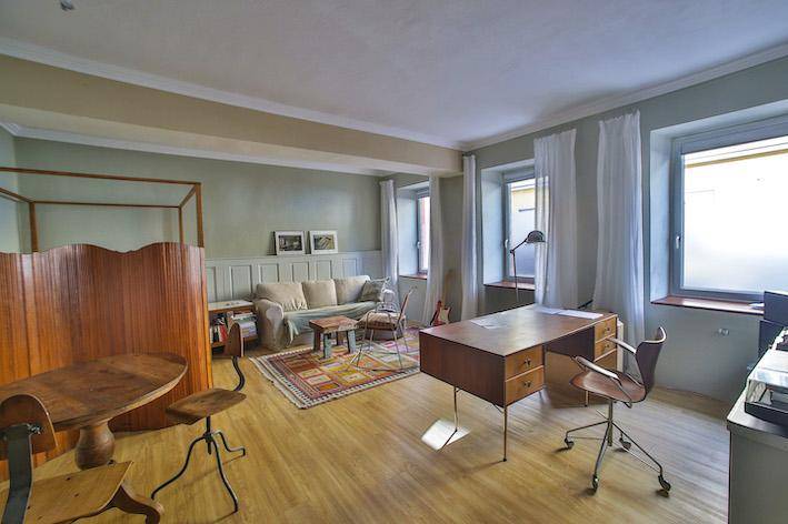 Helles Arbeitszimmer mit Holzmöbeln, Sofa und großen Fenstern.