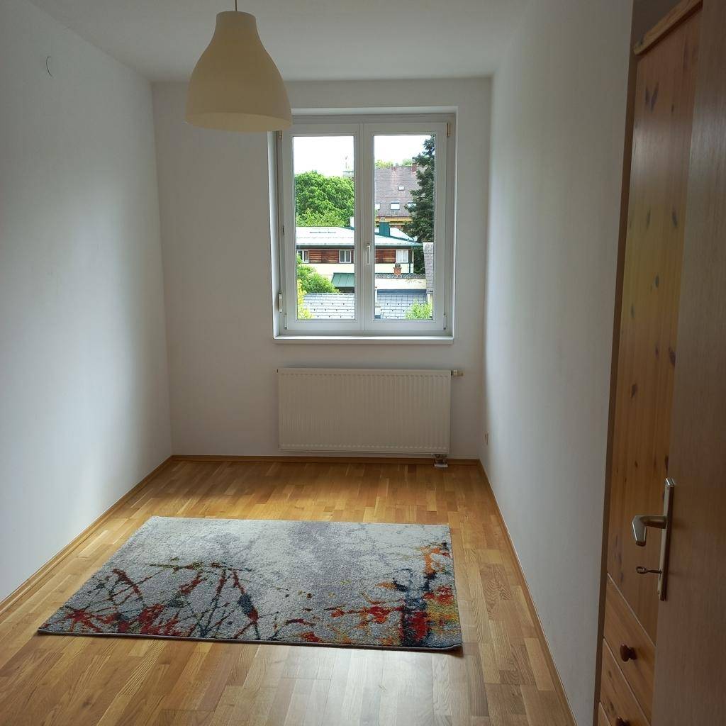 Helles Zimmer mit Holzfußboden, Teppich und einem Fenster mit Blick auf die Umgebung.