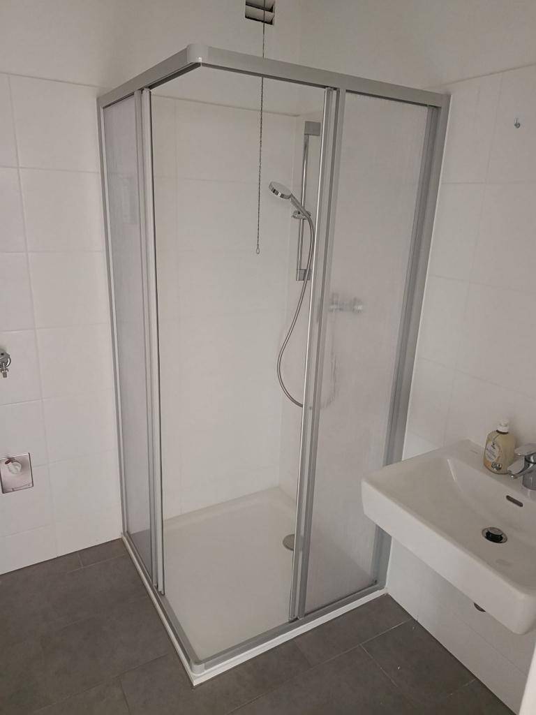 Modernes Badezimmer mit Duschkabine, Waschbecken und hellen Fliesen.