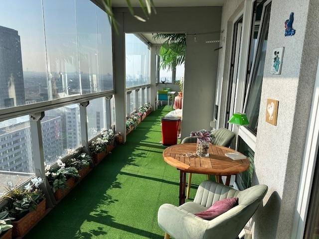Langer Balkon mit moderner Glasfront, Kunstrasen, bequemen Sitzgelegenheiten und weitem Stadtblick.