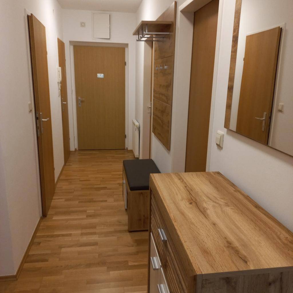 Geräumiger Flur mit Holzfußboden, Kommode und Garderobe, die einen einladenden Eingangsbereich schaffen.