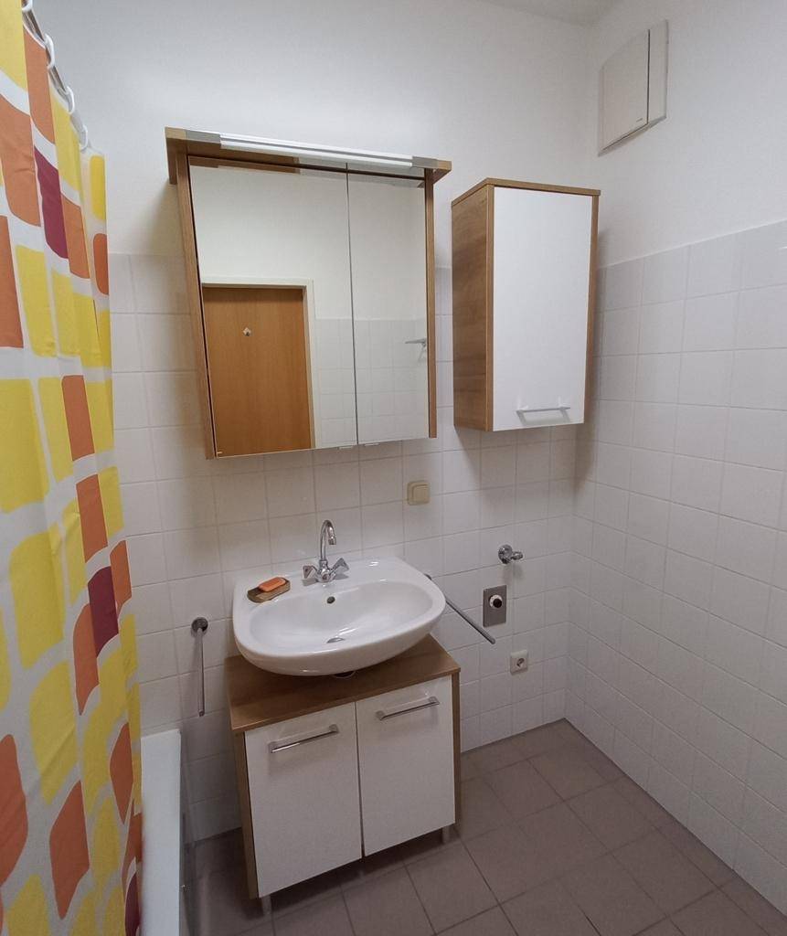 Funktionales Badezimmer mit Waschbecken, Spiegelschrank und Duschvorhang, hell gefliest.