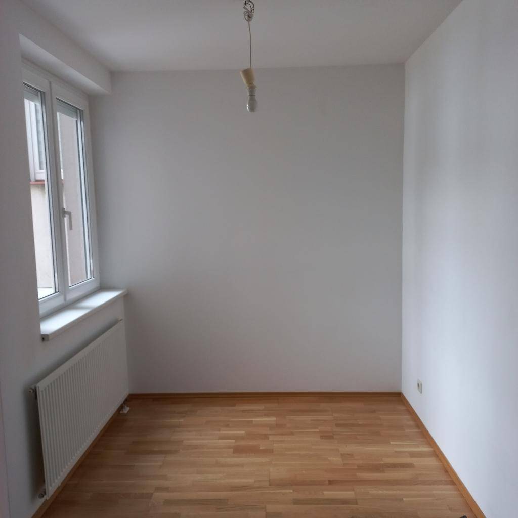 Leeres Zimmer mit Holzfußboden und weiß gestrichenen Wänden, bereit zur individuellen Gestaltung.