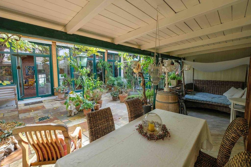 Überdachte Terrasse mit Esstisch, Pflanzen und gemütlicher Sitzecke im Freien.