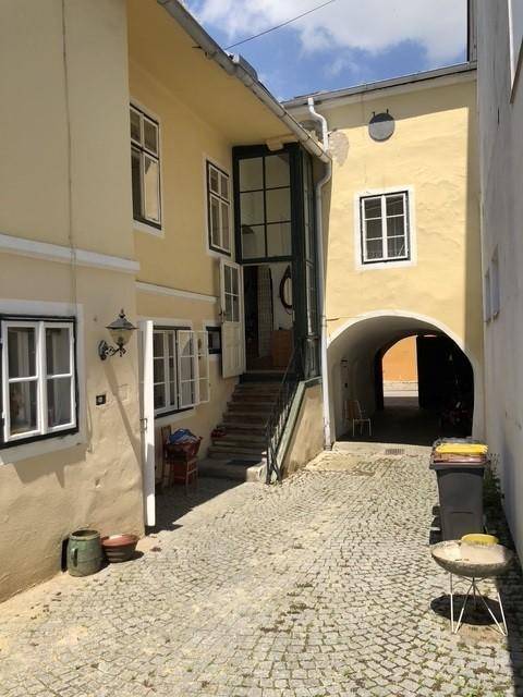 Sonniger Innenhof mit Kopfsteinpflaster, gelben Fassaden und einem Durchgang zu weiteren Gebäuden.