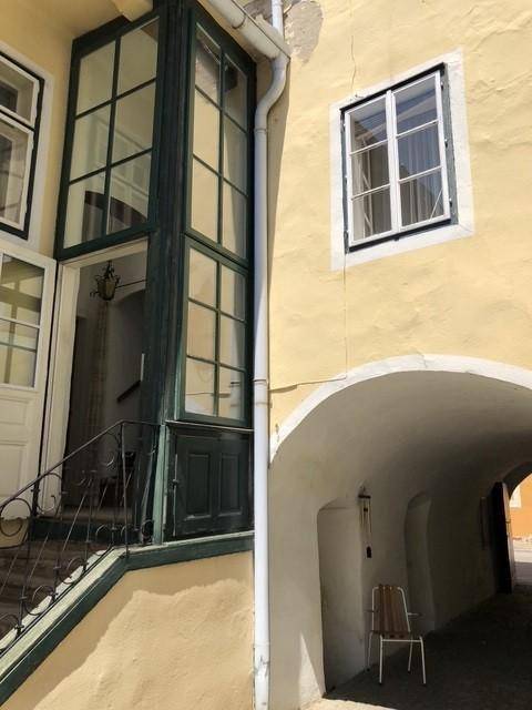 Detailansicht einer gelben Fassade mit einem markanten grünen Glaserker und einem gewölbten Durchgang.