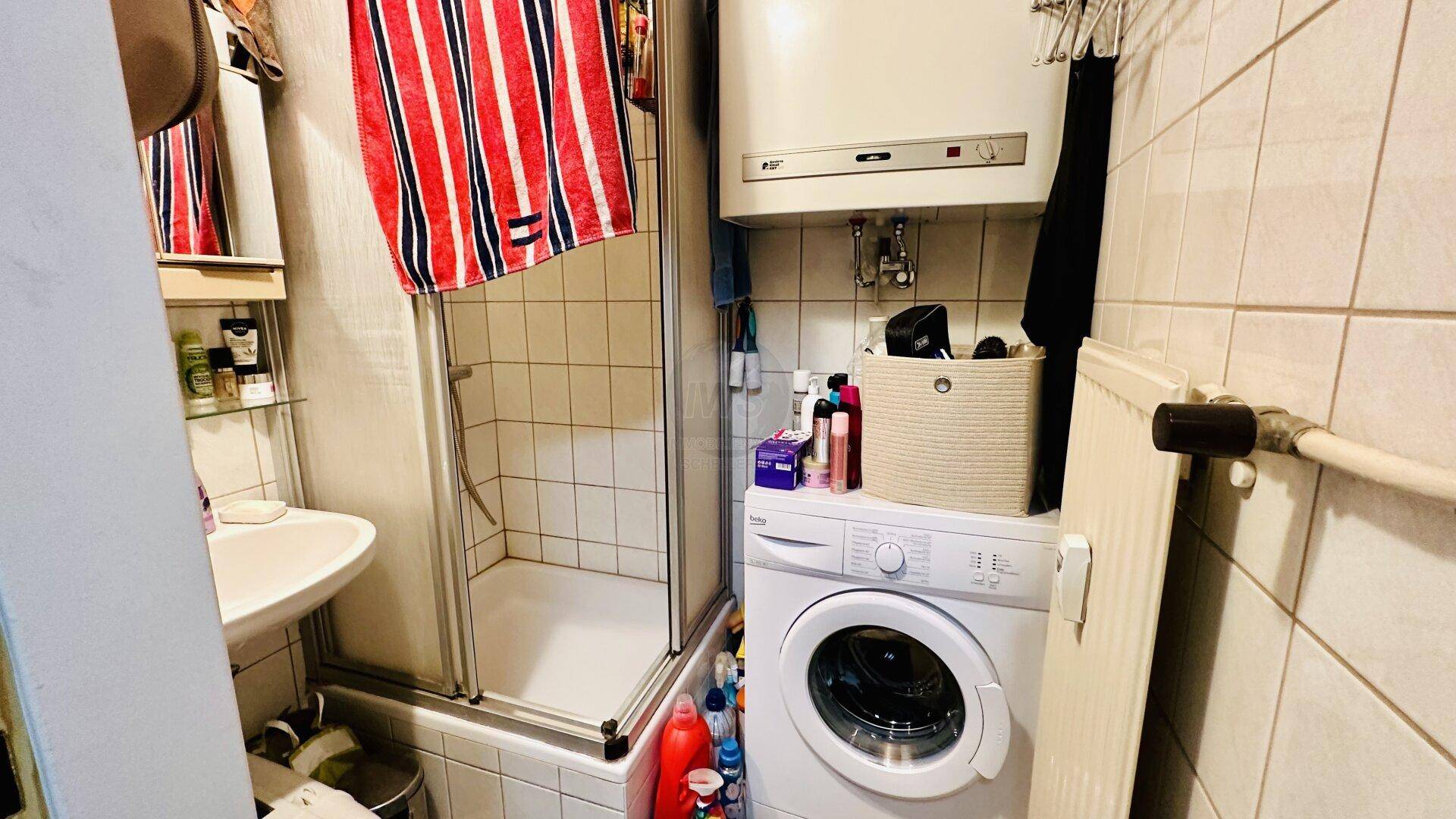 Kleines Badezimmer mit Dusche, Waschmaschine und Boiler, praktisch eingerichtet.