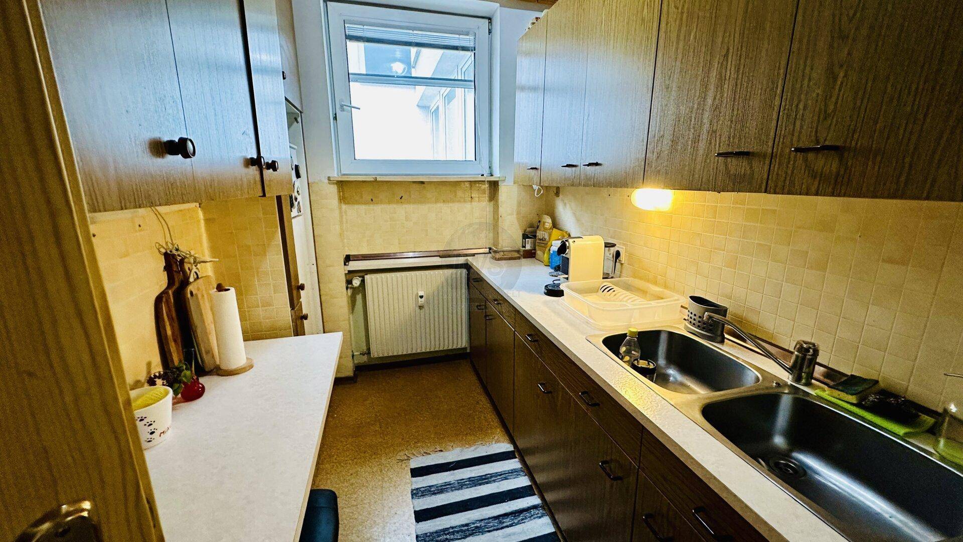 Funktionale Küche mit Holzschränken, Fliesenrückwand und Fenster, in gutem Zustand.