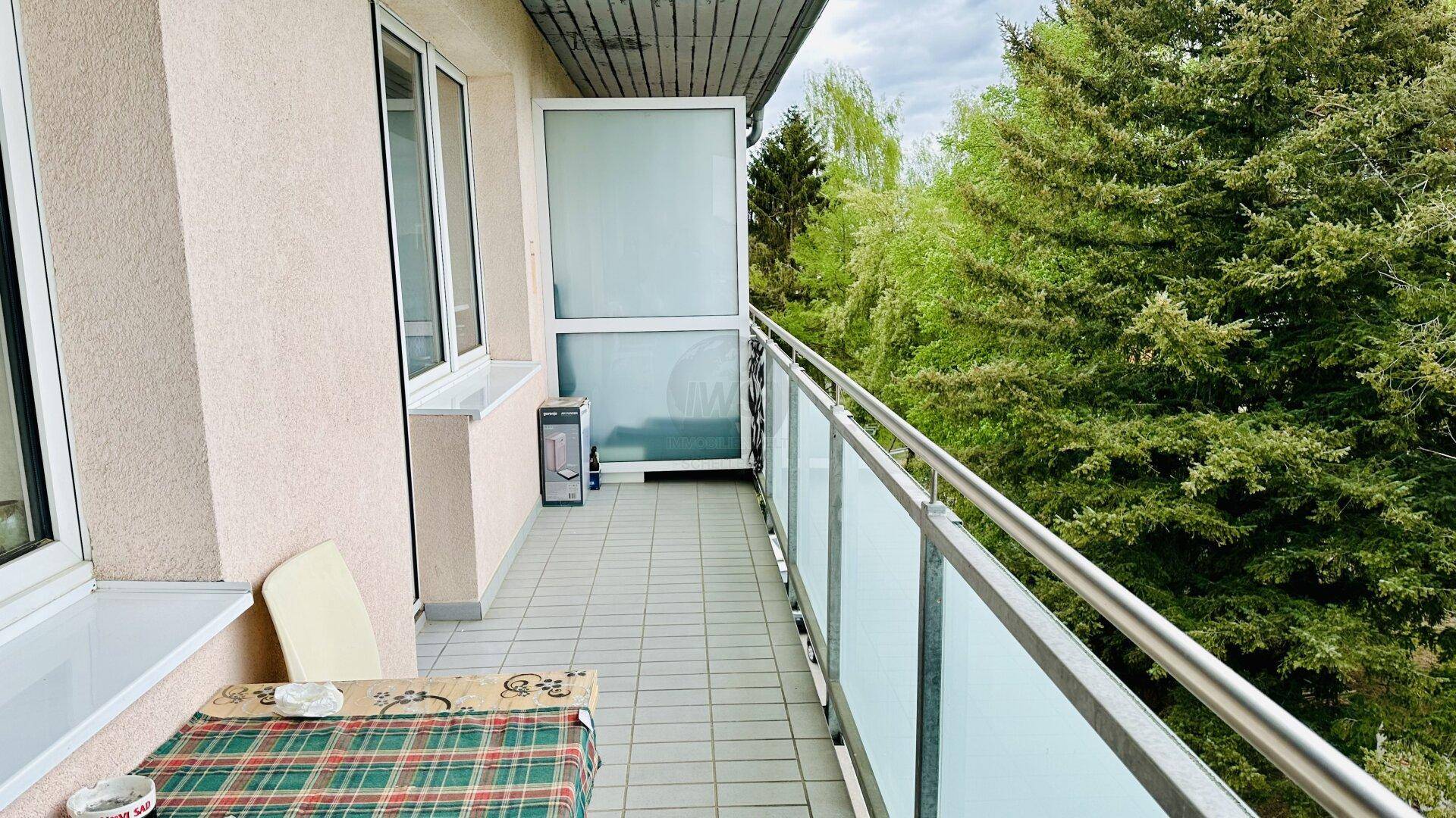 Langer Balkon mit Fliesenboden, Glasgeländer und Blick ins Grüne.