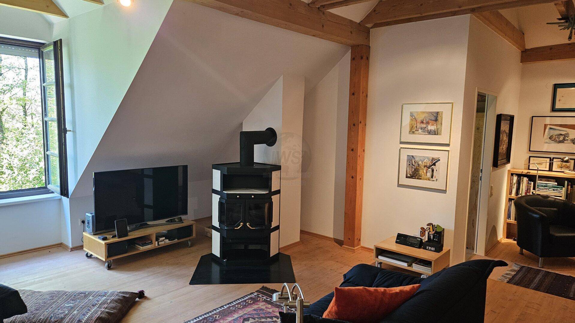 Gemütliches Wohnzimmer im Dachgeschoss mit Kaminofen, Holzbalken und schrägen Wänden.