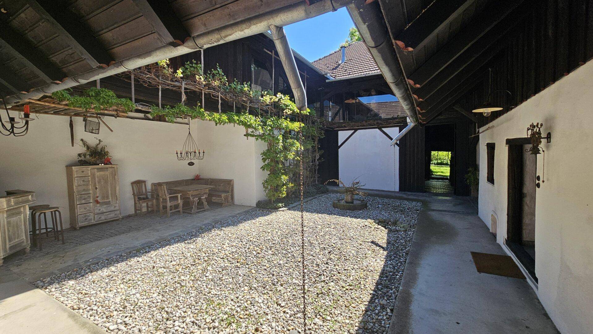 Geräumiger Innenhof mit Kiesboden, überdachtem Bereich und rustikalen Sitzgelegenheiten.