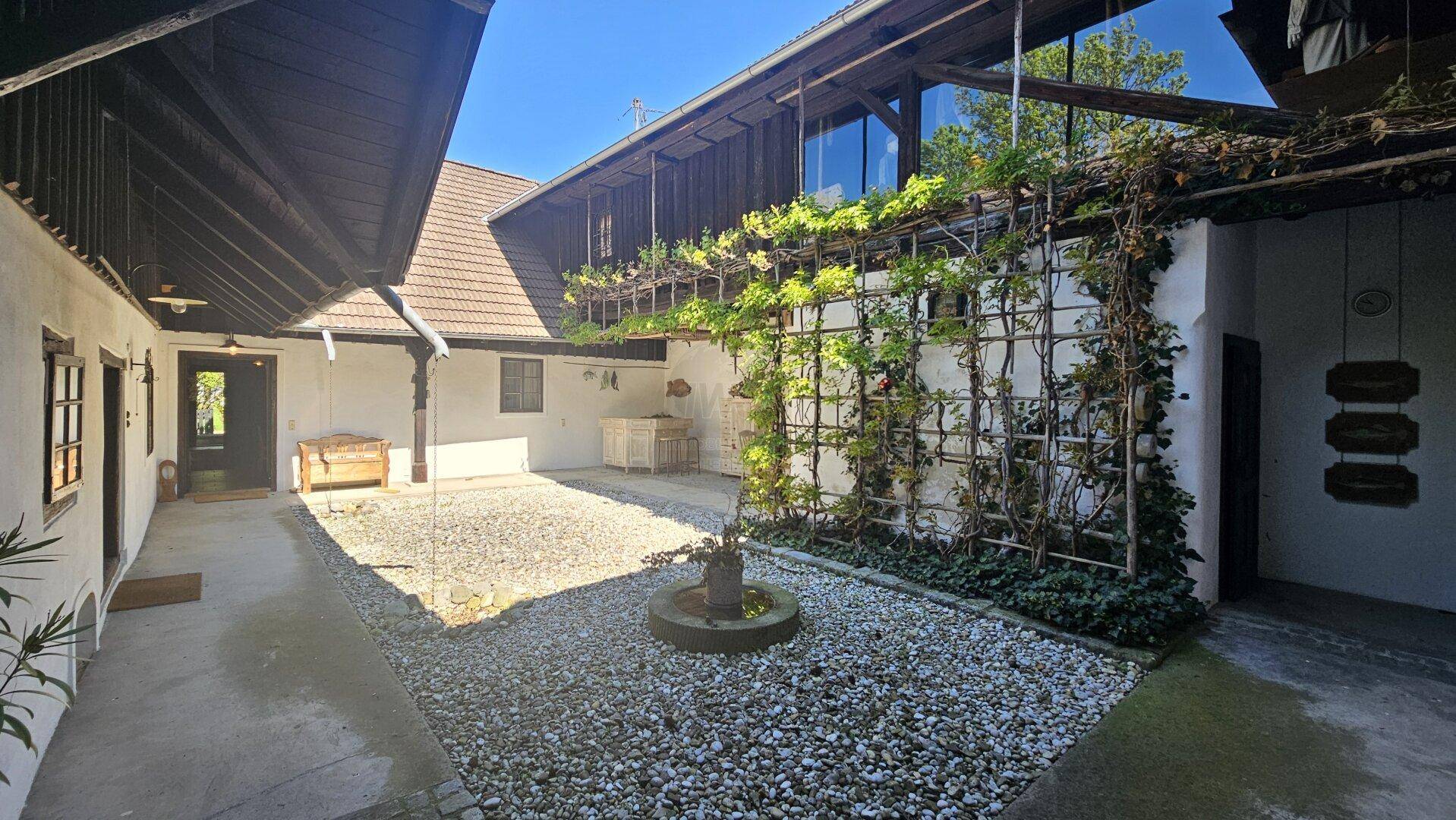 Sonniger Innenhof mit Kiesboden, begrünten Rankgittern und traditioneller Architektur.