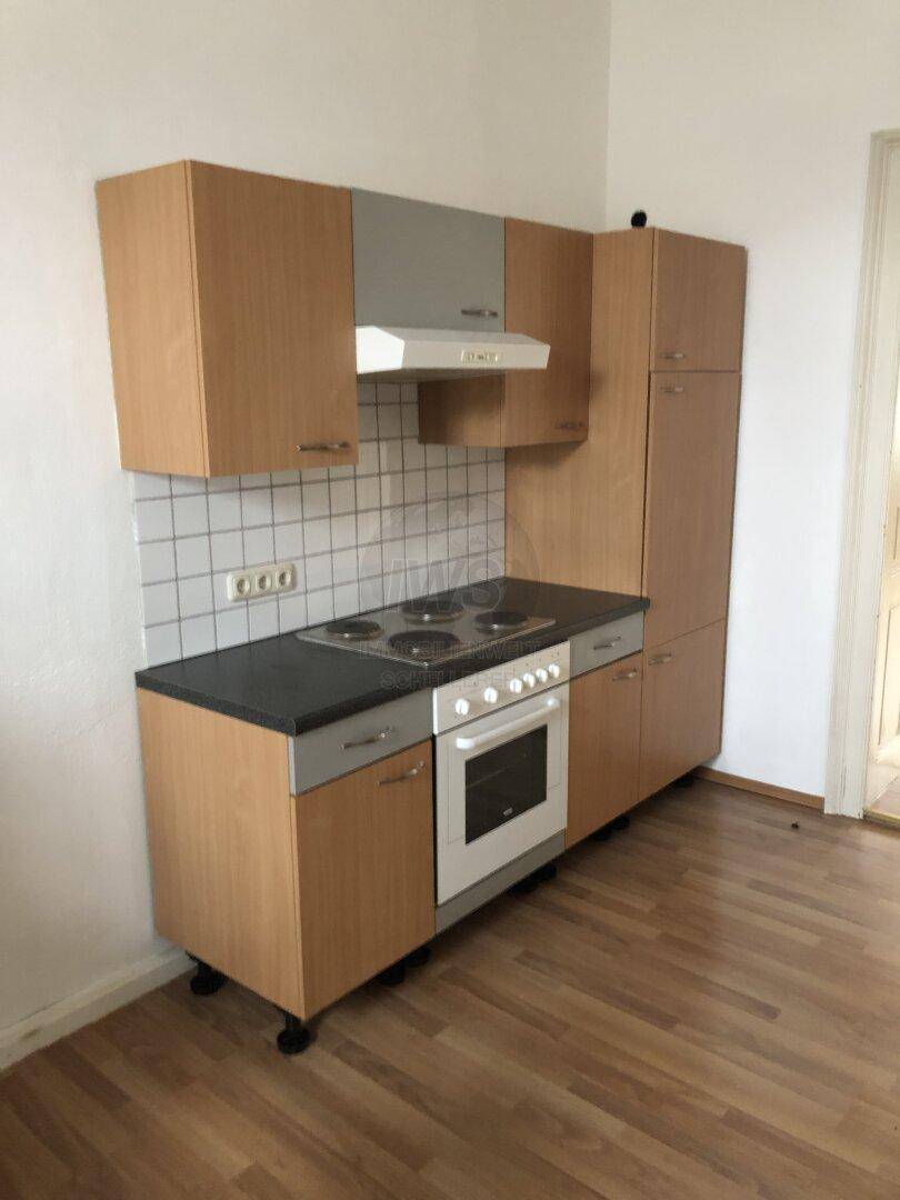 Kompakte Einbauküche mit Holzschränken, schwarzer Arbeitsplatte, Elektroherd und weißem Fliesenspiegel.