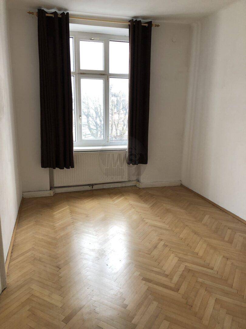 Schlafzimmer mit Fischgrätparkett, weißen Wänden und Fenster mit dunklen Vorhängen für Privatsphäre.