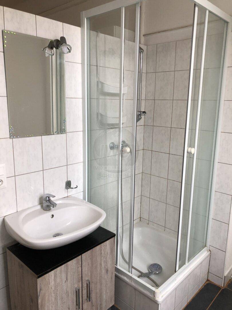 Badezimmer mit weiß gefliesten Wänden, Duschkabine, Waschbecken mit Unterschrank und Spiegel.