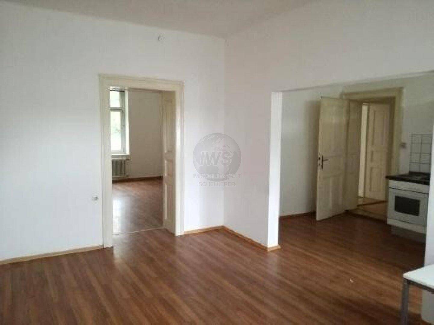 Offener Wohnbereich mit Holzdielenboden und Zugang zu weiteren Zimmern, inklusive Küchenblick.