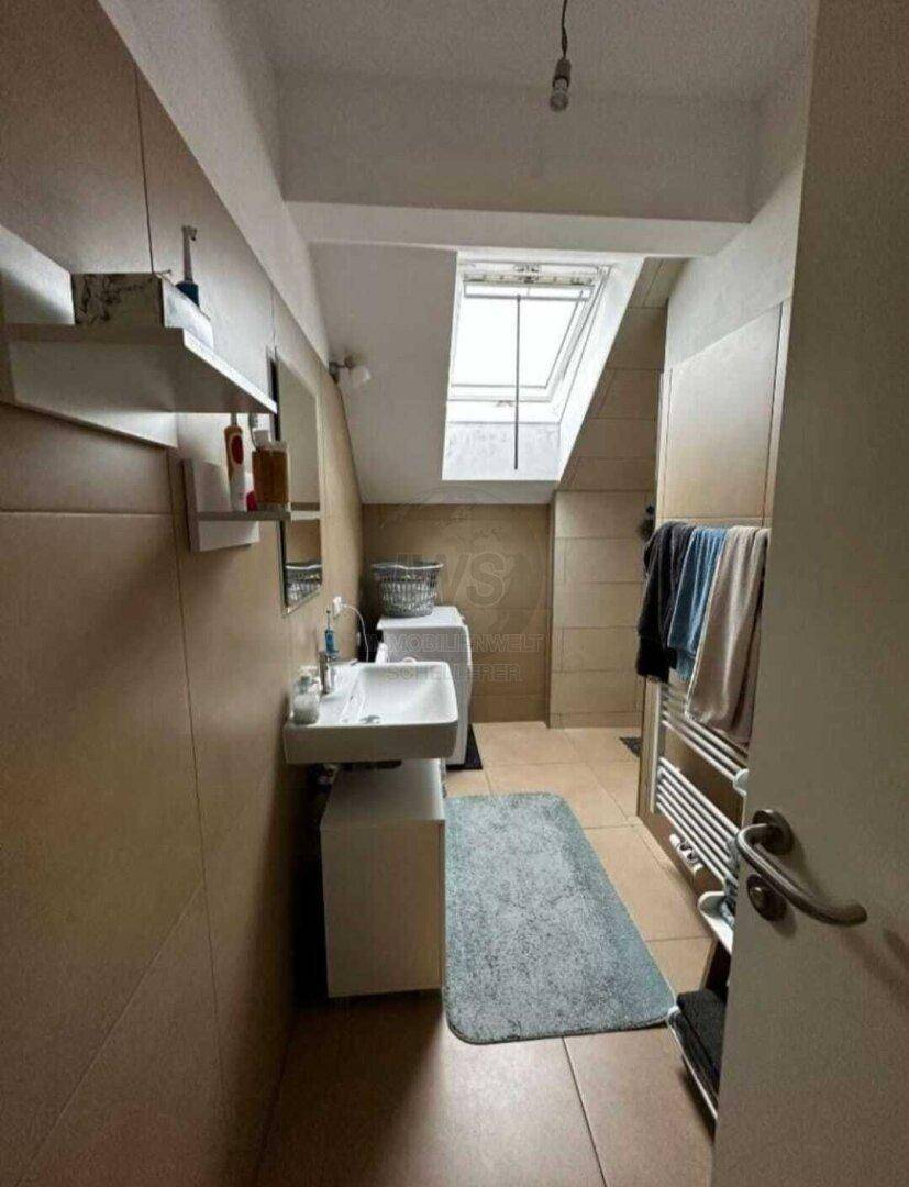 Modernes Badezimmer im Dachgeschoss mit Dachfenster, Waschbecken und Waschmaschine.