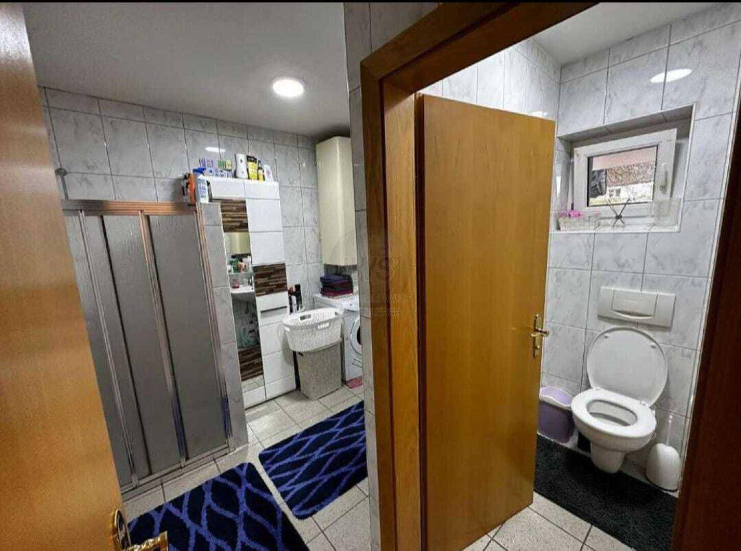 Gefliestes Badezimmer mit Duschkabine, Toilette und kleinem Fenster.