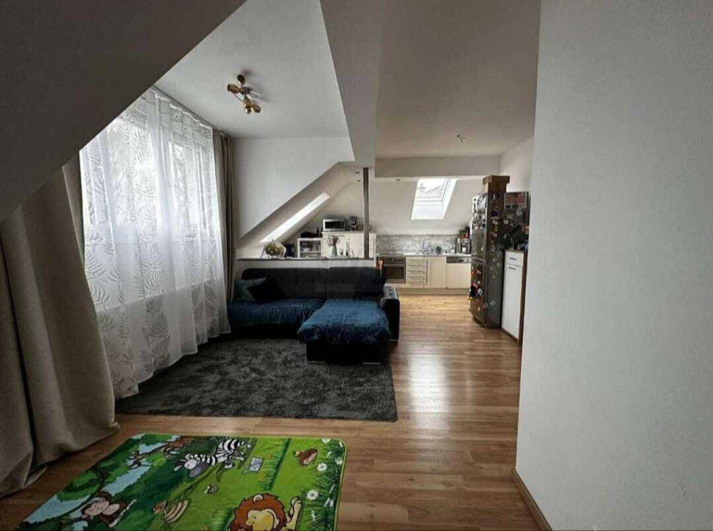 Offener Wohnbereich im Dachgeschoss mit Holzboden und integrierter Küche.