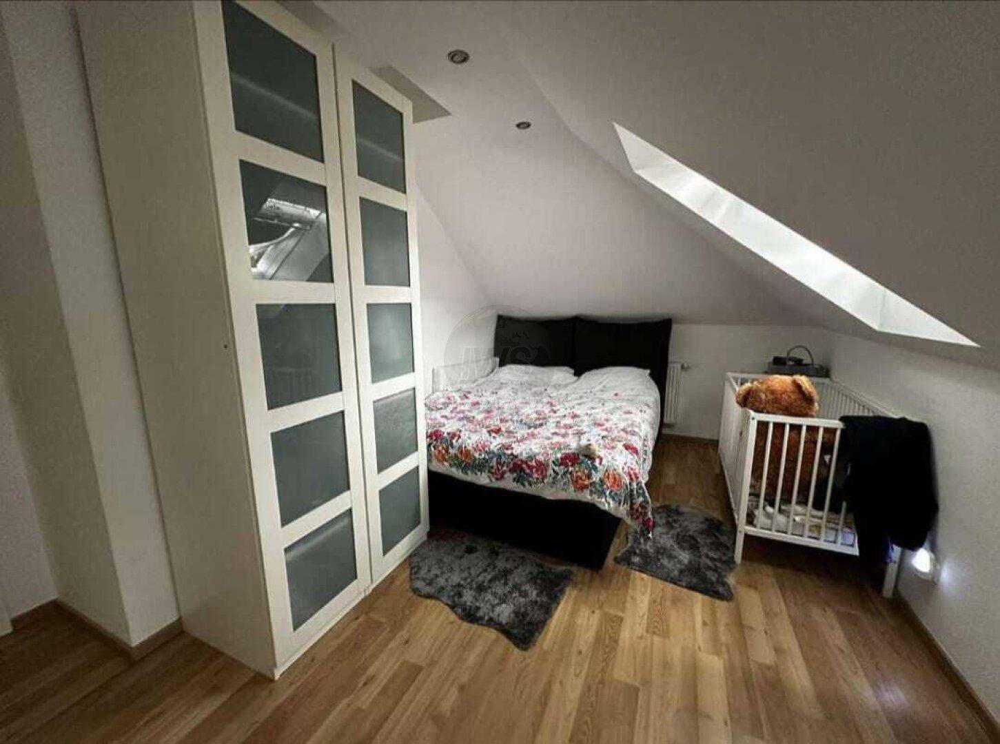Schlafzimmer im Dachgeschoss mit Holzboden, Doppelbett und Babybett.